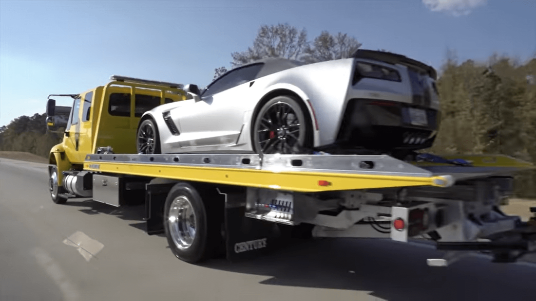 Yellow flatbed tow truck towing silver Corvette