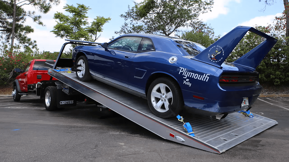 Red flatbed tow truck towing blue Plymouth Barracuda