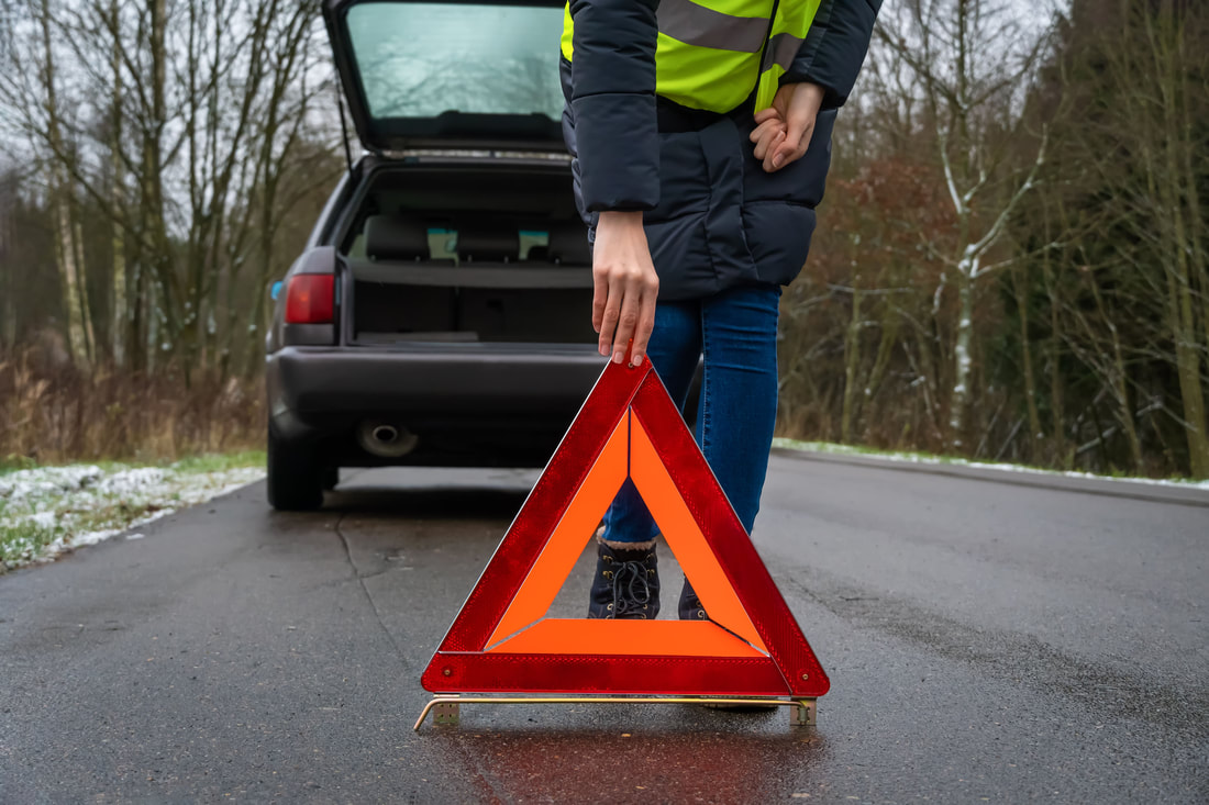 Lady placing orange reflective road hazard warning triangle signs behind her car