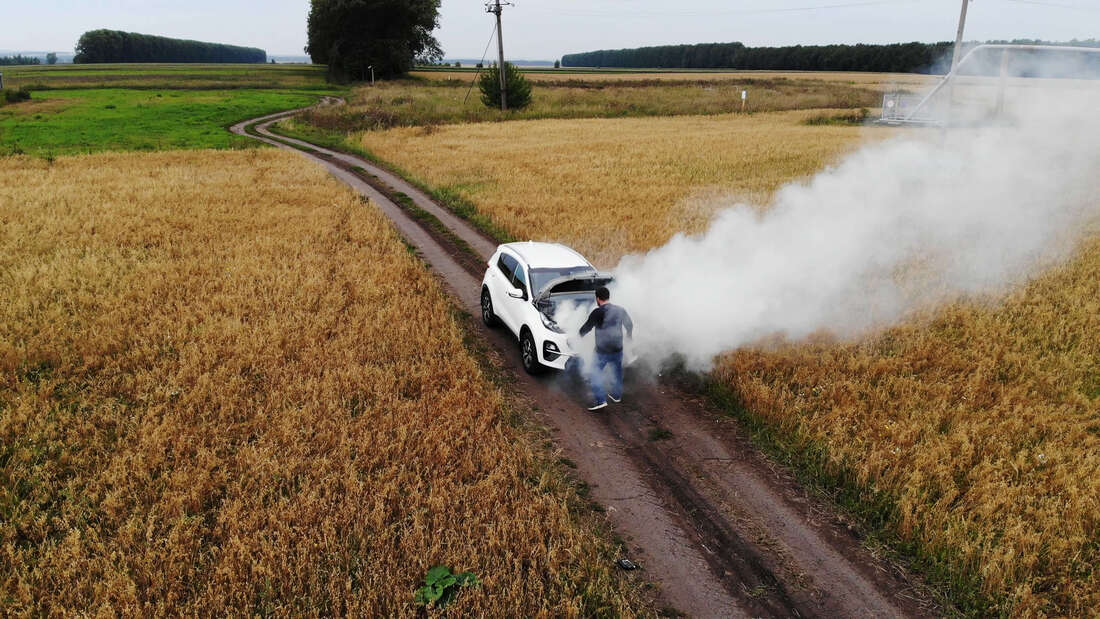 Over heated car on dirt road in farm field with smoke pouring from under the hood
