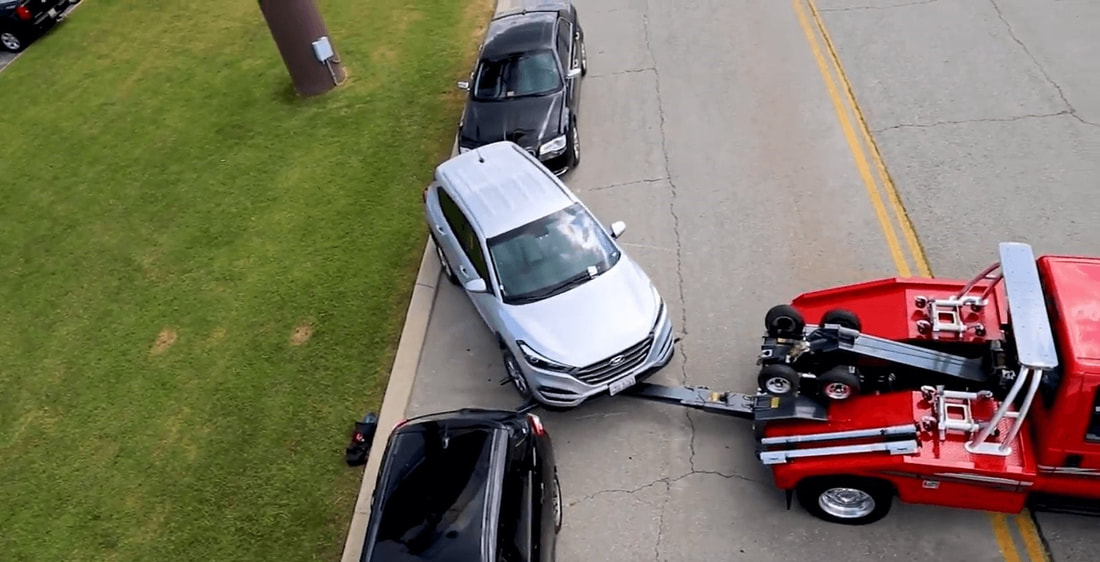 Red tow truck moving parallel parked car between two cars 