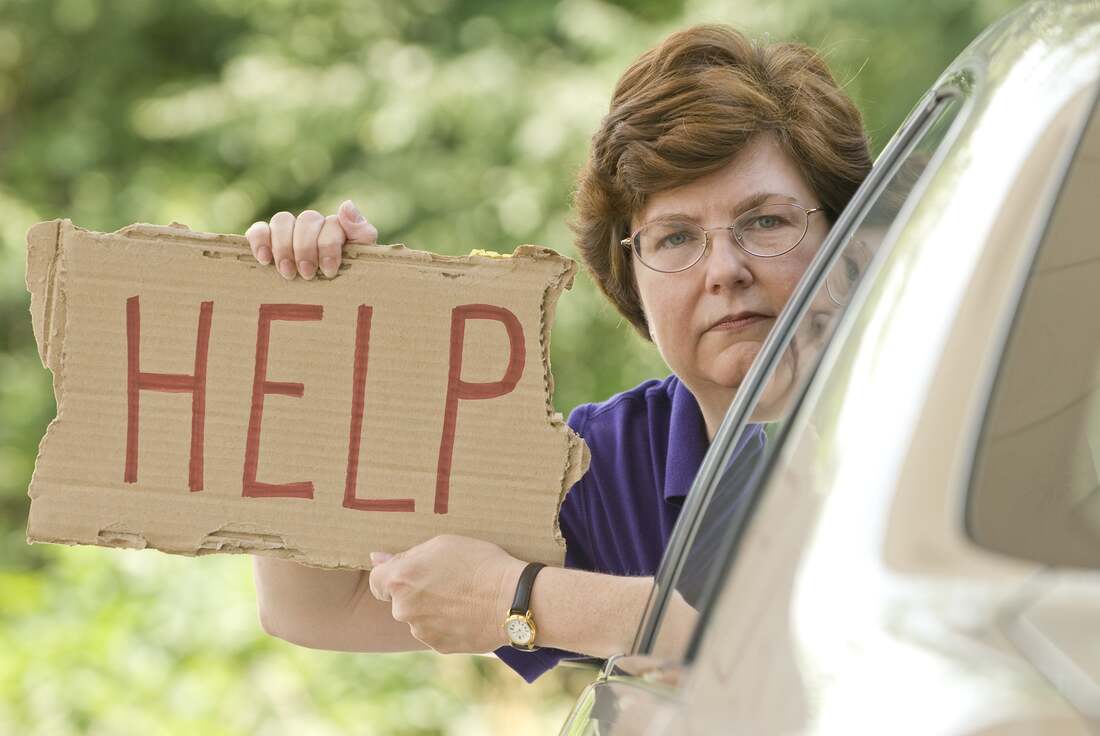 Woman in car holding sign that says HELP need of roadside assistance